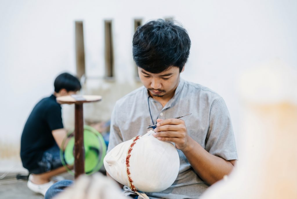 ช่างรุ่นใหม่กำลังใช้เหล็กจารตกแต่งลวดลายบนชิ้นงานหัวโขน สะท้อนการสืบสานภูมิปัญญาสกุลช่างเมืองเพชรสู่คนรุ่นใหม่